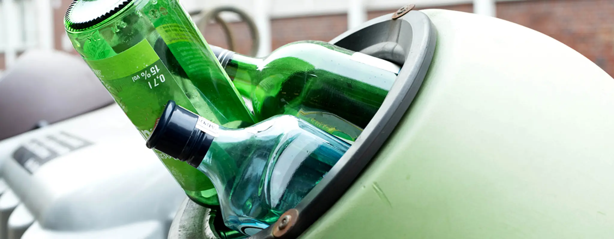 Grüne Glasflaschen ragen aus einem Altglascontainer