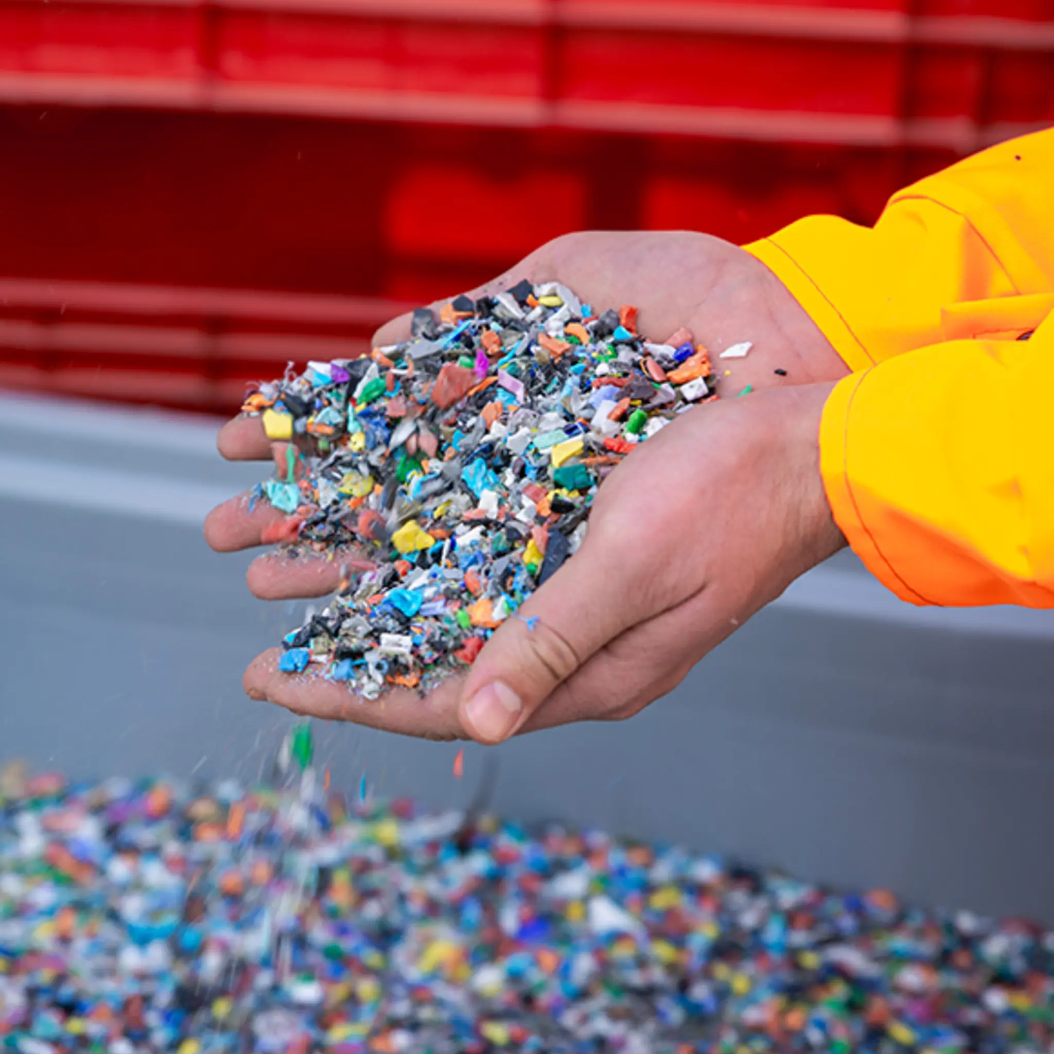 Zwei Hände schöpfen kleine, bunte Plastikpartikel aus einer Kiste