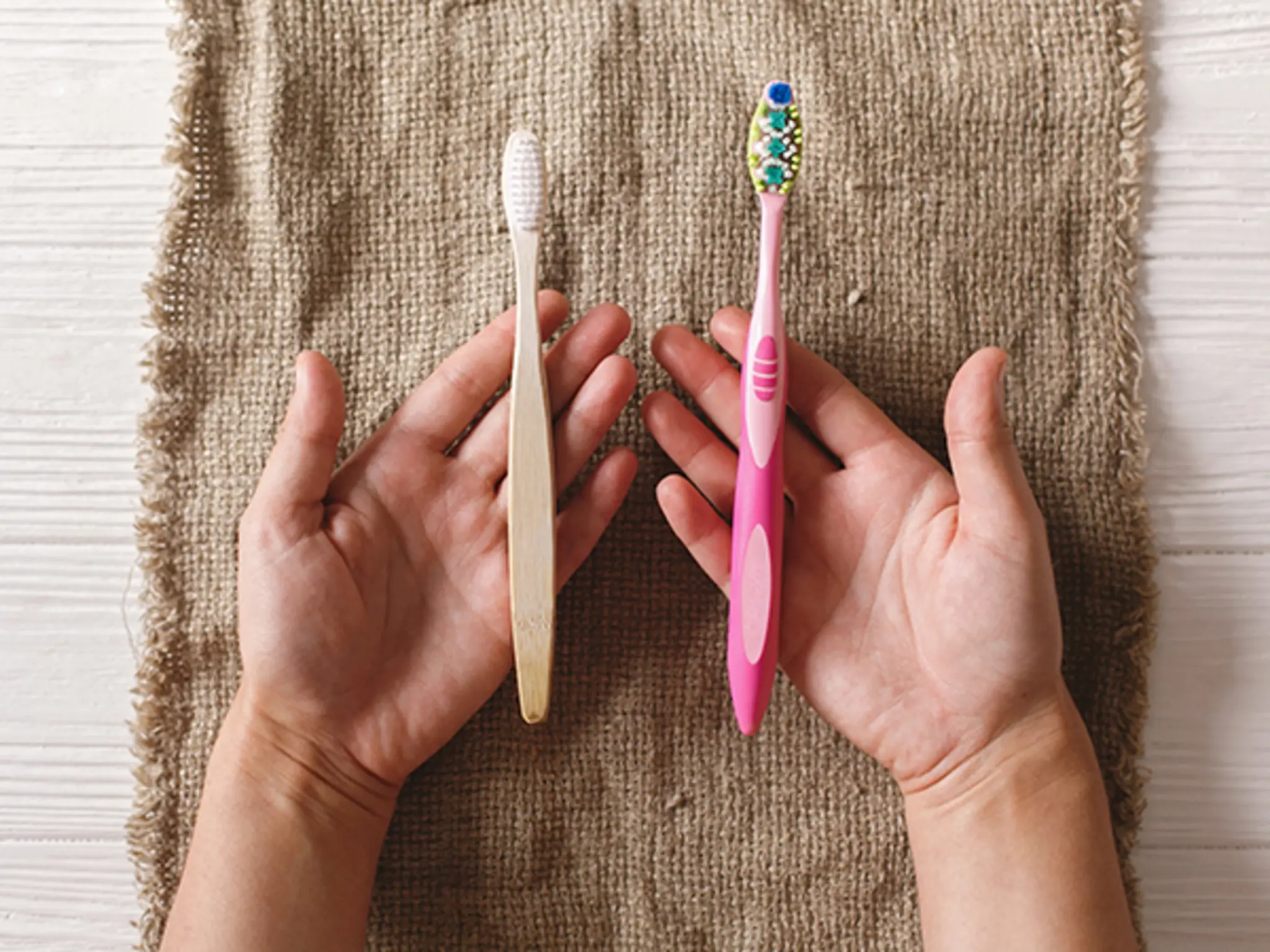 Zwei Hände, die eine Bambus-Zahnbürste und eine Plastik-Zahnbürste halten