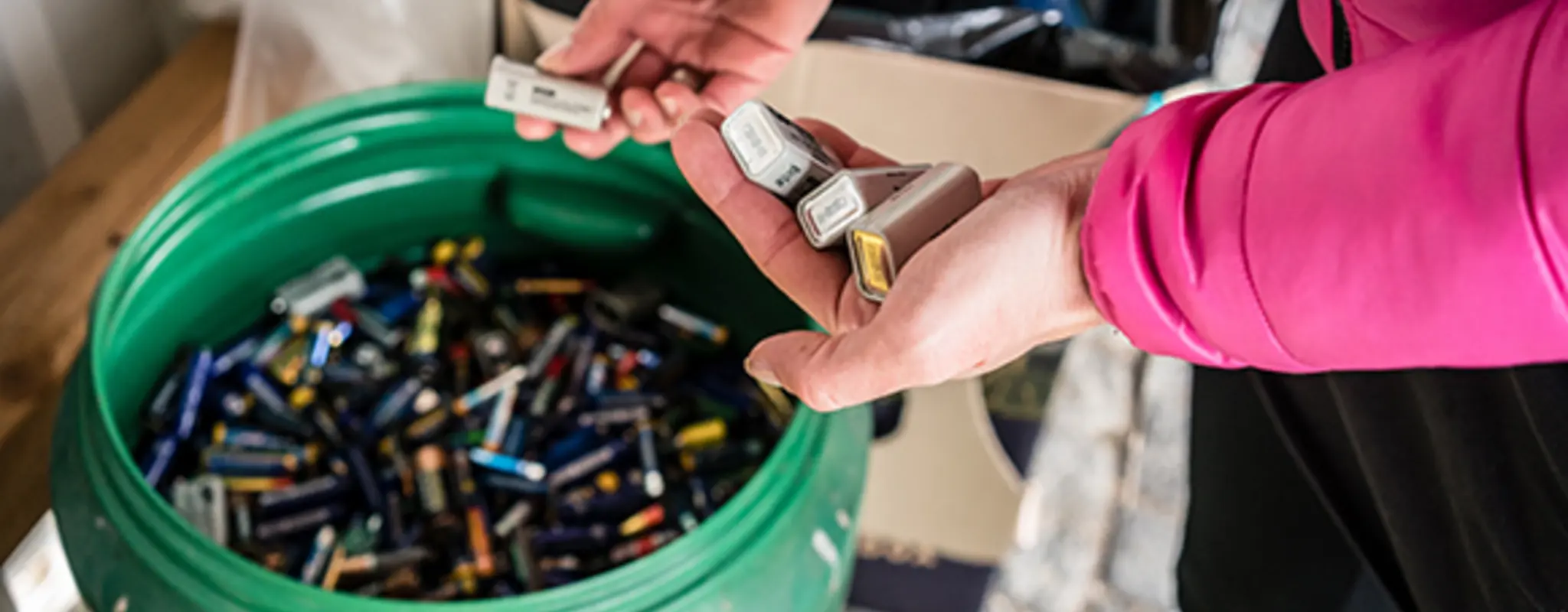 Eine Person in Freizeitkleidung wirft Batterien in einen Sammelbehälter 