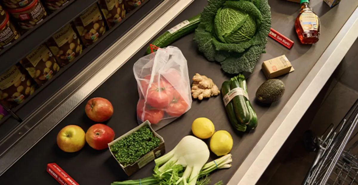 Verschiedene unverpackte Obst- und Gemüsesorten liegen auf einem Kassenband.
