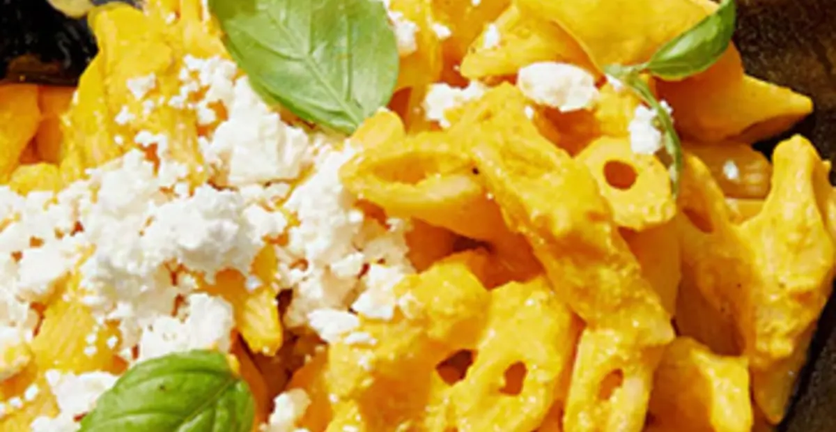 Ein Teller mit Kürbis Feta Pasta steht auf einem gedeckten Tisch. 
