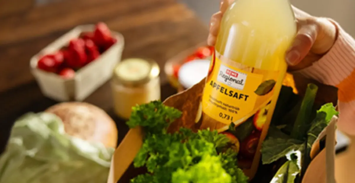 Eine Person nimmt REWE Regional Apfelsaft aus einer REWE Papiertüte.