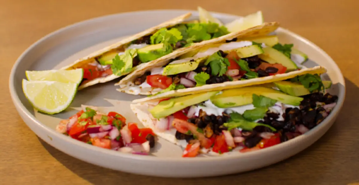 Ein Teller Tacos – gefüllt mit schwarzen Bohnen, Tomaten, roten Zwiebeln, Avocado und frischen Kräutern.