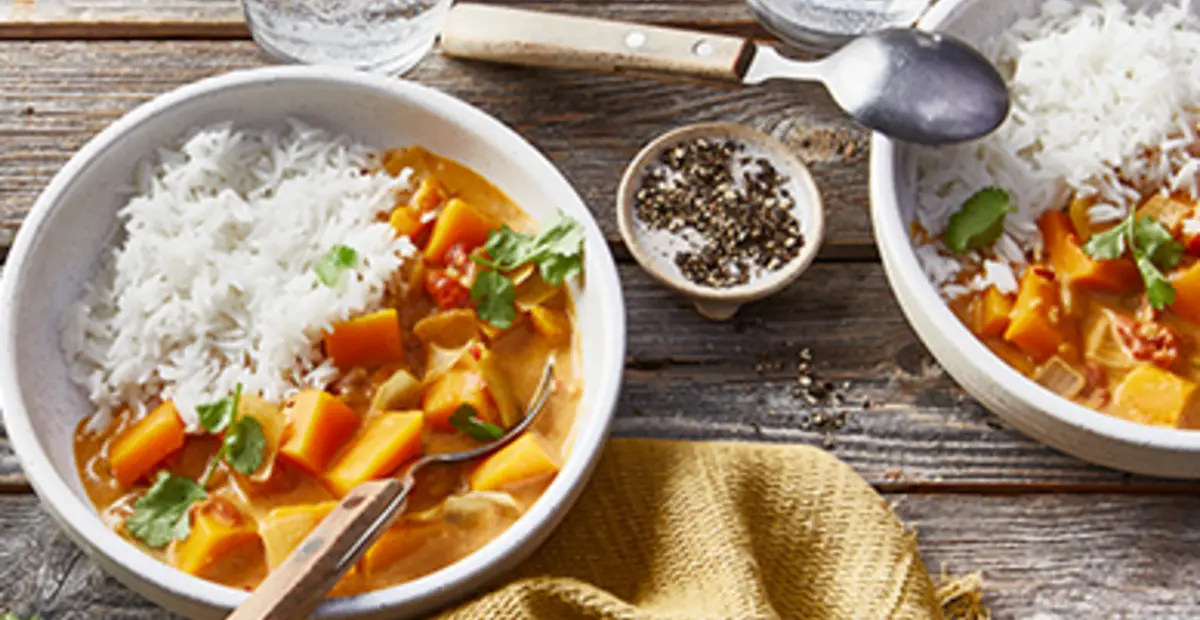 Ein Teller pikantes Kürbis-Curry steht auf einem Holztisch.