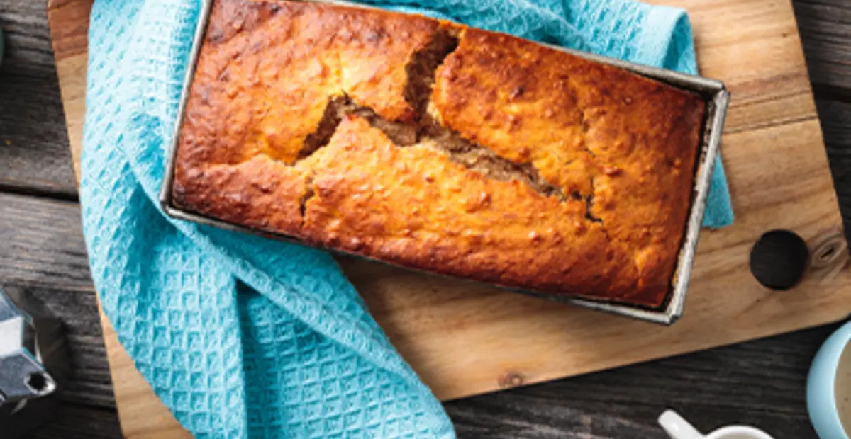 Ein veganes Bananenbrot steht auf einem gedeckten Kaffeetisch.
