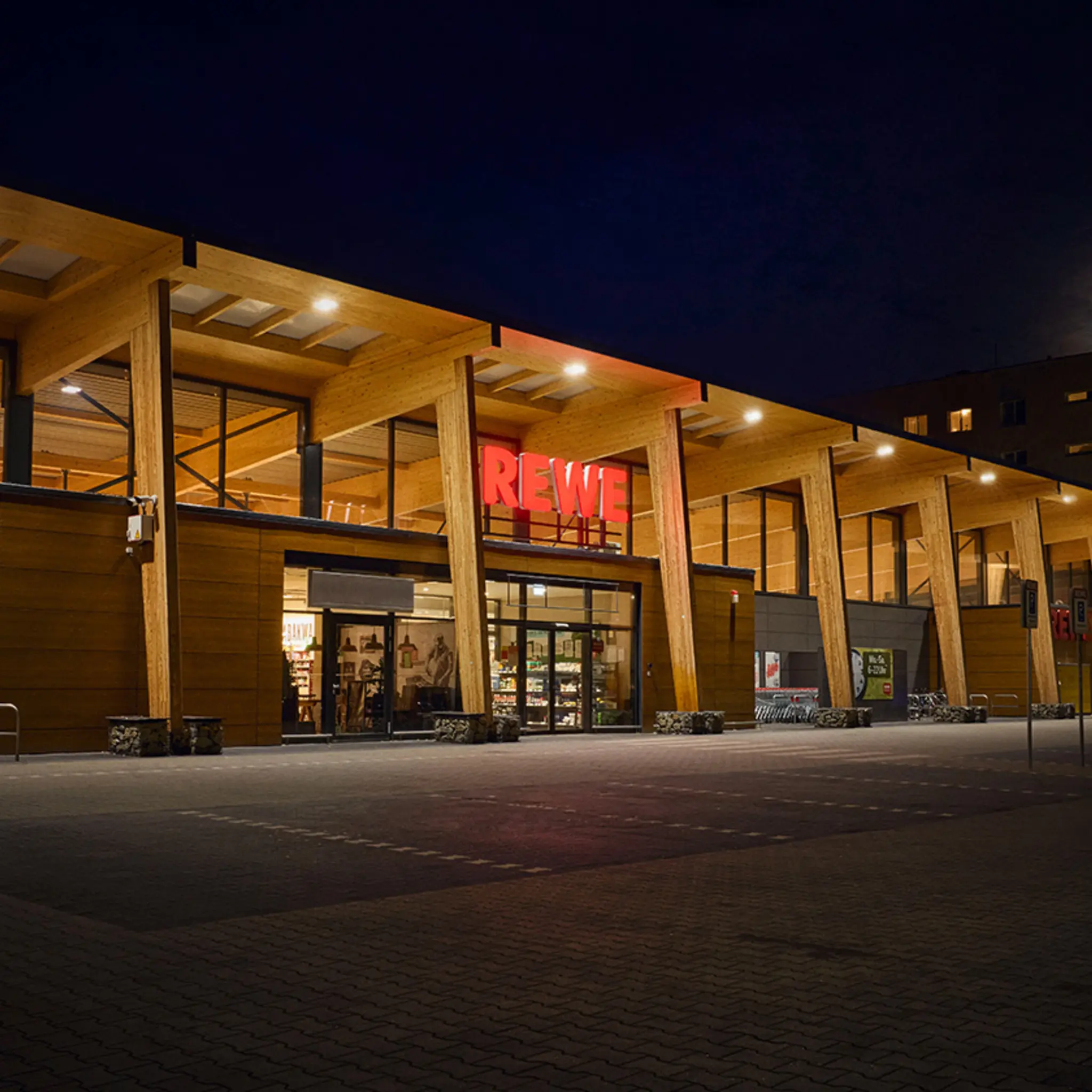 Ein hell erleuchtetes REWE Green Building bei Dunkelheit.