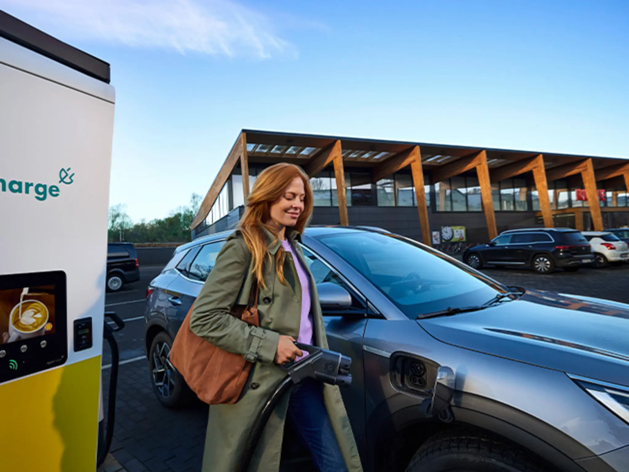 Der Parkplatz eines nachhaltigeren REWE Green Buildings. Eine Kundin lädt ihr E-Auto mit grünem Strom.