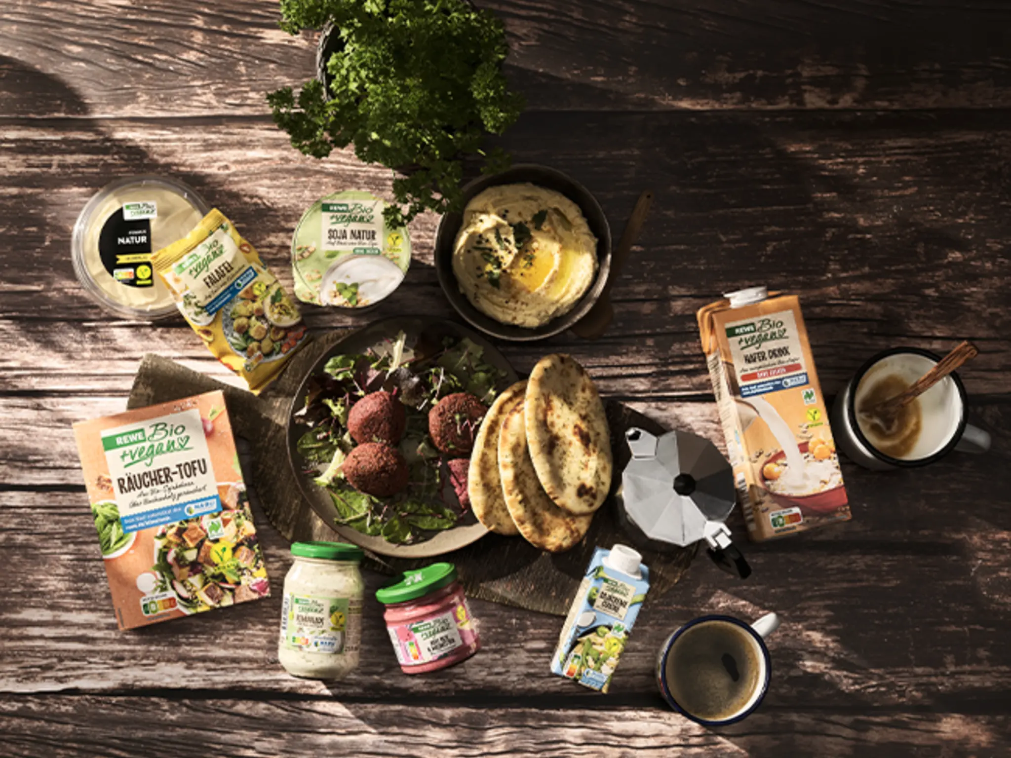 Verschiedene REWE Bio und REWE Bio + vegan Produkte liegen auf einem rustikalen Holztisch. Mit dem Kauf unterstützt du den NABU Klimafonds.