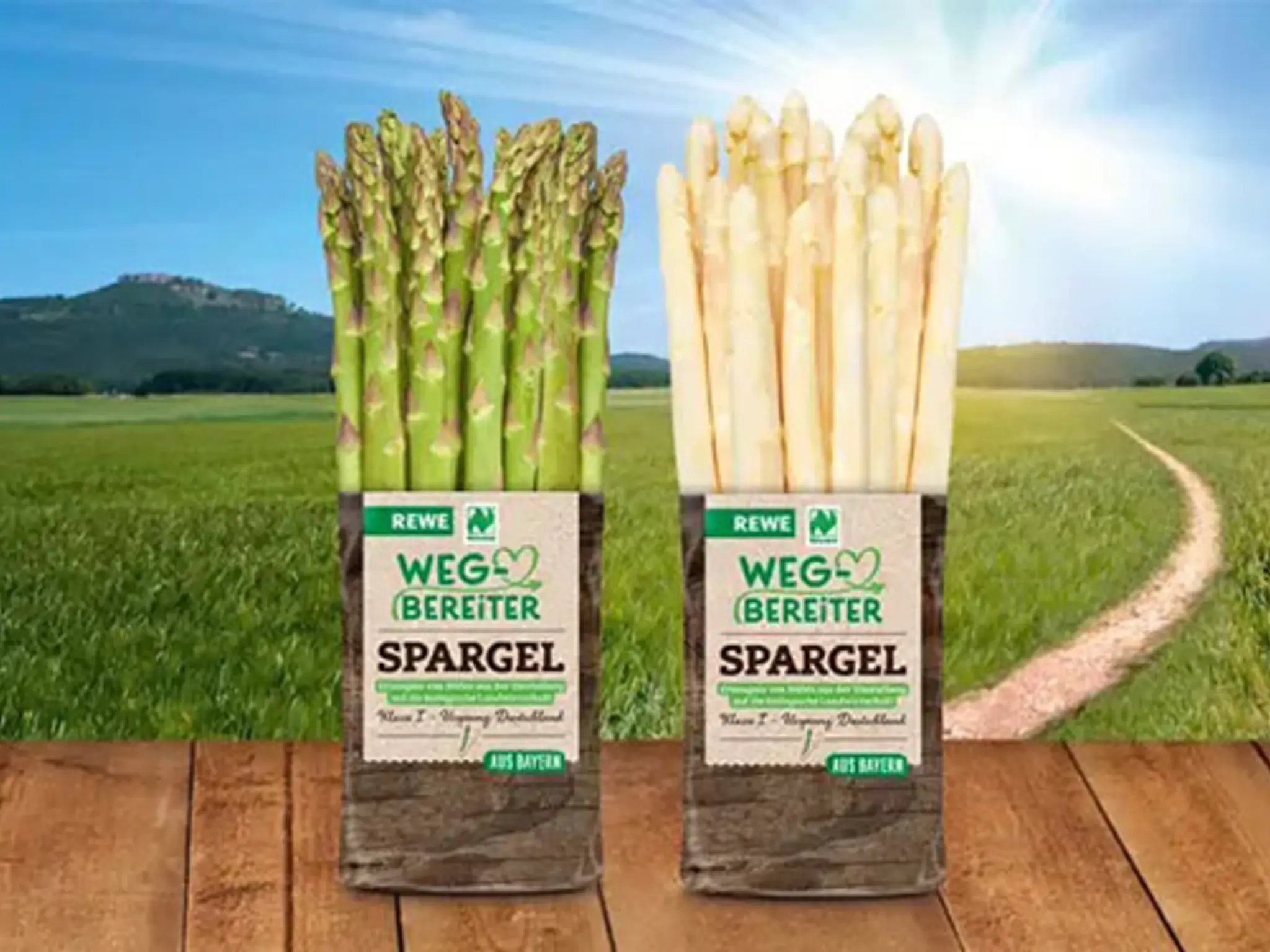 Je ein Bund grüner und weißer Spargel. Beide tragen eine Banderole mit dem Schriftzug „Wegbereiter“. Im Hintergrund erkennt man ein sonniges Feld.