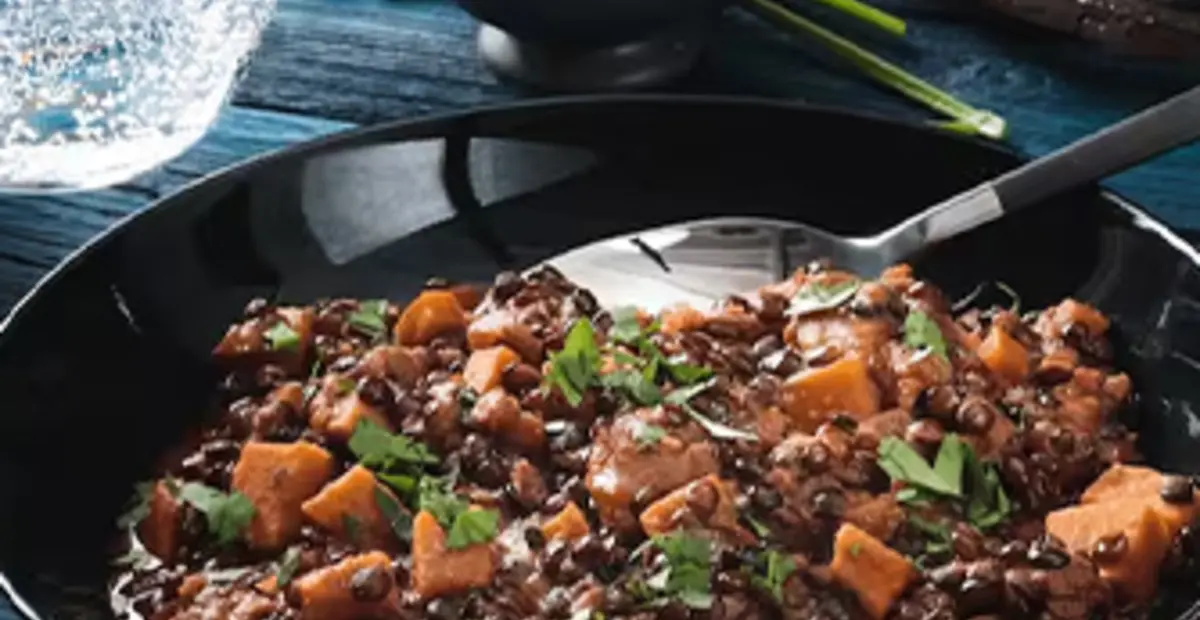 Zwei Teller mit veganem Belugalinsen-Curry stehen neben dem leeren Topf auf einem Tisch.