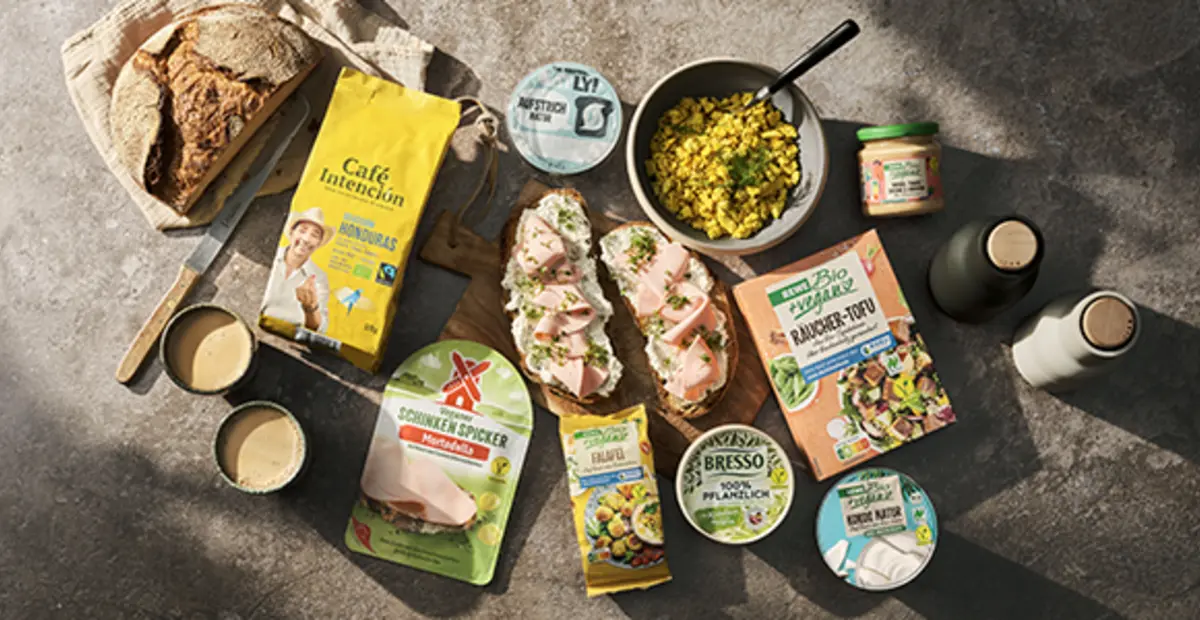 Verschiedene REWE Bio + vegan Produkte stehen auf einem Holztisch.