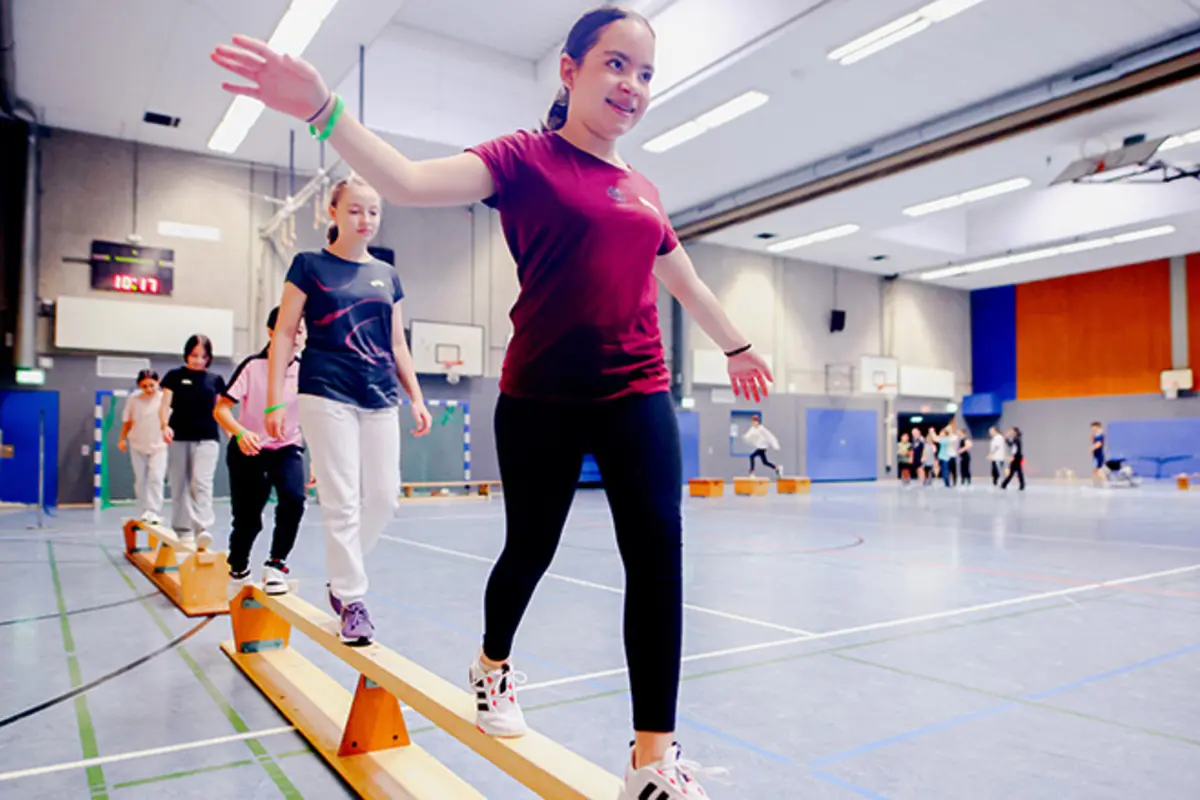 Mehrere Jugendliche mit und ohne Behinderung balancieren auf umgedrehten Sportbänken. 