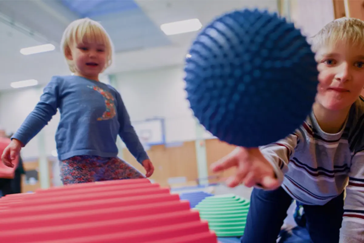 Ein balancieren in einem Geschicklichkeitsparcours. Eines wirft einen Gymnastikball in Richtung Kamera. 
