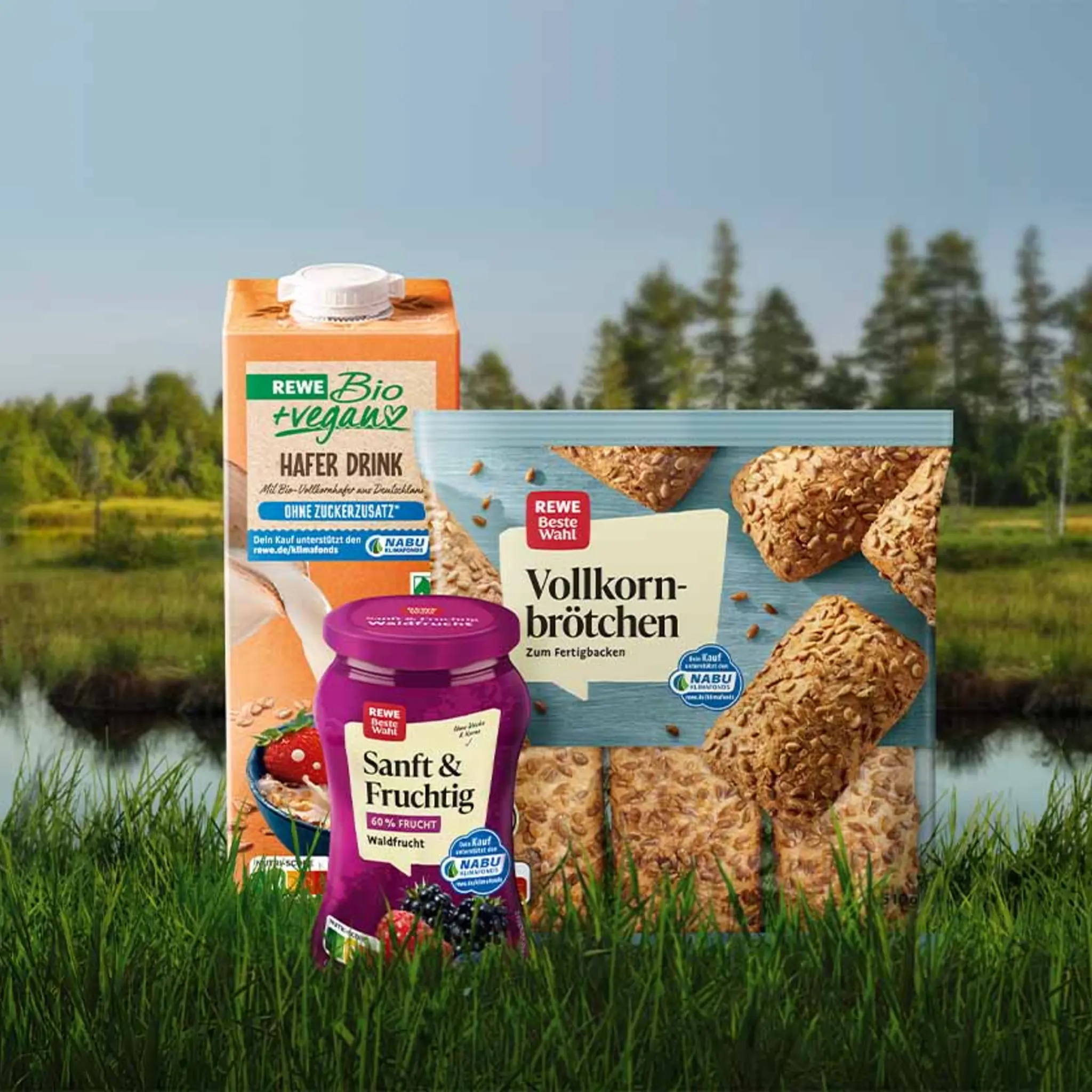 Eine Packung REWE Bio + vegan Hafer Drink und eine Packung REWE Beste Wahl Milde Genießerscheiben vegan vor einem naturbelassenen Moor im Hintergrund.