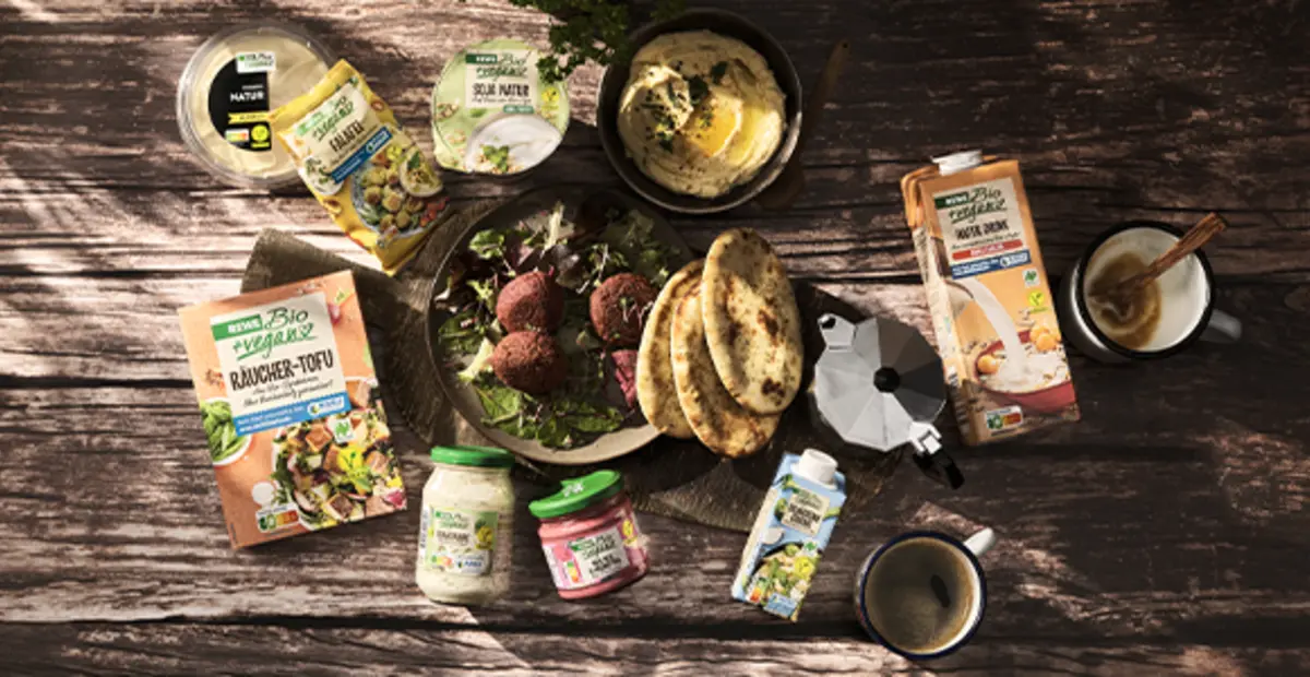 Verschiedene REWE Bio und REWE Bio + vegan Produkte liegen auf einem rustikalen Holztisch. Mit dem Kauf unterstützt du den NABU-Klimafonds.