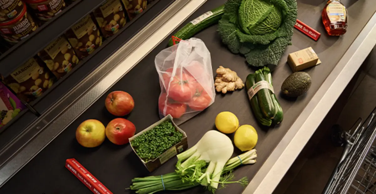 Verschiedene REWE Eigenmarken-Produkte in optimierten Verpackungen liegen auf einem Kassenband.