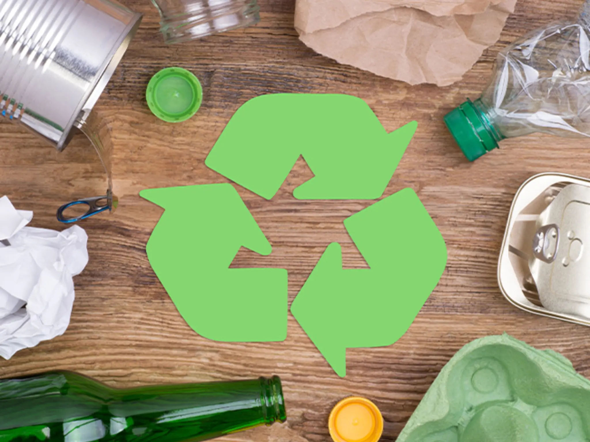 Auf einem Tisch liegen alte Verpackungen aus unterschiedlichen Materialien. In der Mitte ist das Recycling-Symbol zu sehen. 