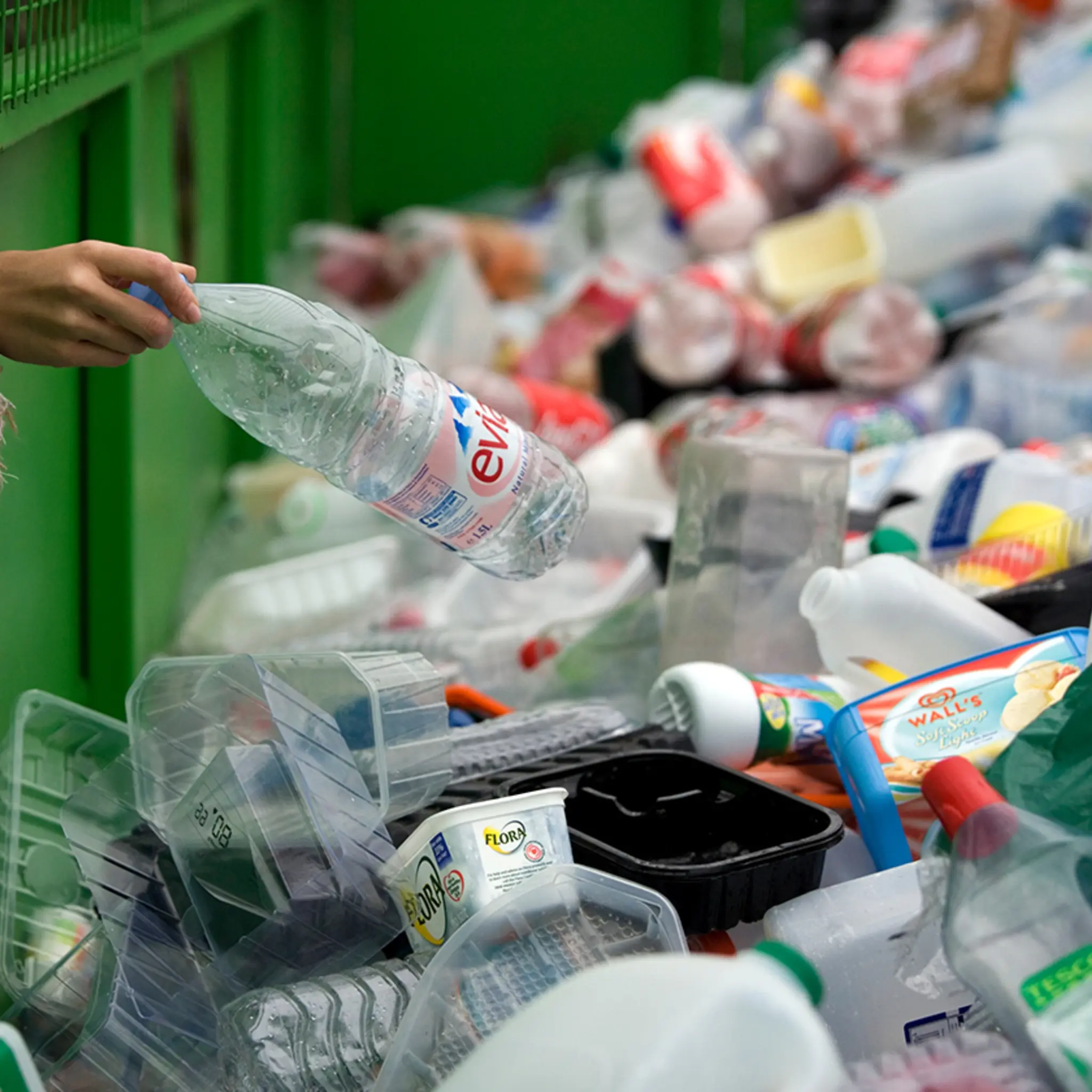 Eine Person wirft eine leere Plastikflasche in einen Container mit anderen Kunststoffverpackungen.