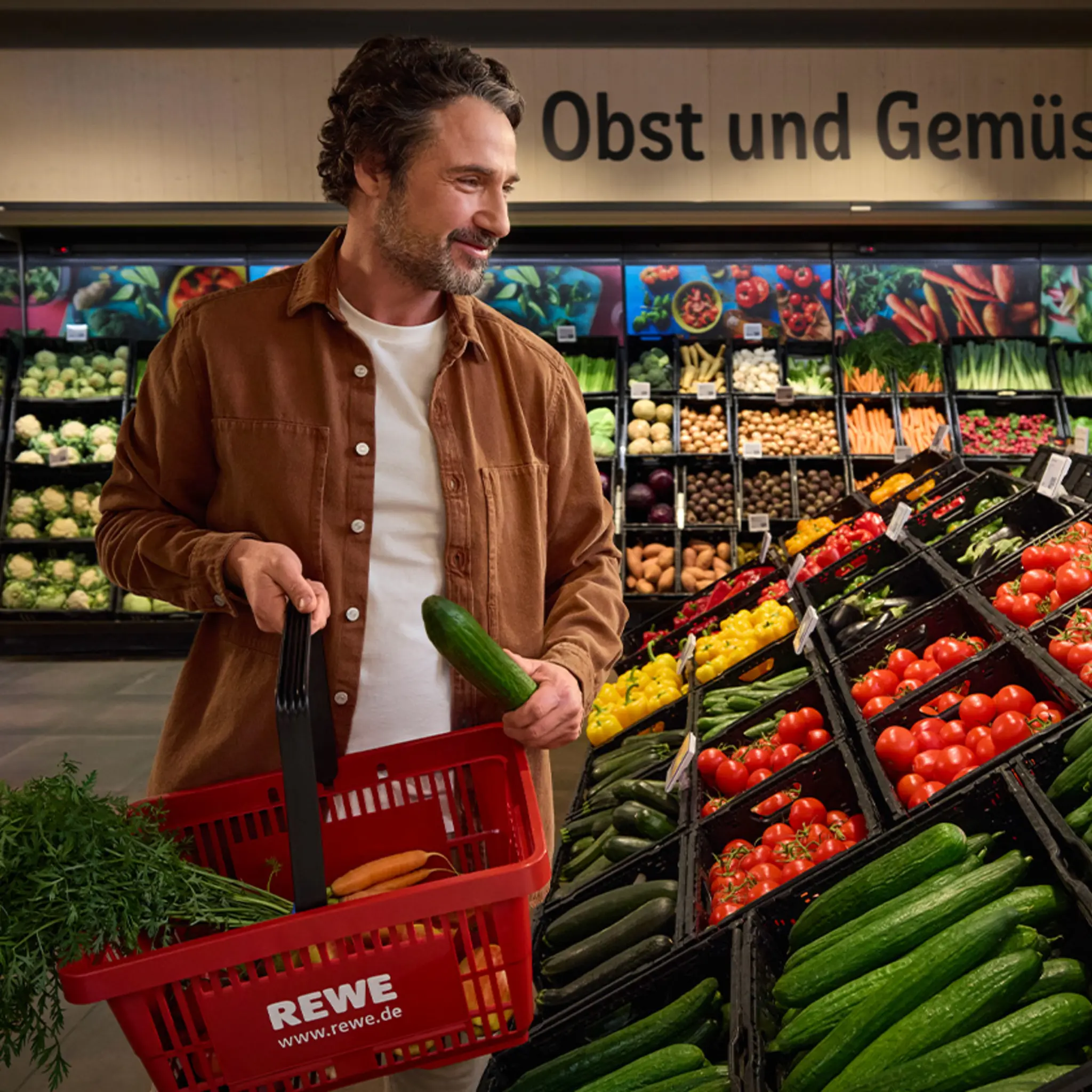 Ein Kunde in seinem REWE Markt. Er legt unverpacktes Obst und Gemüse in den Einkaufskorb.