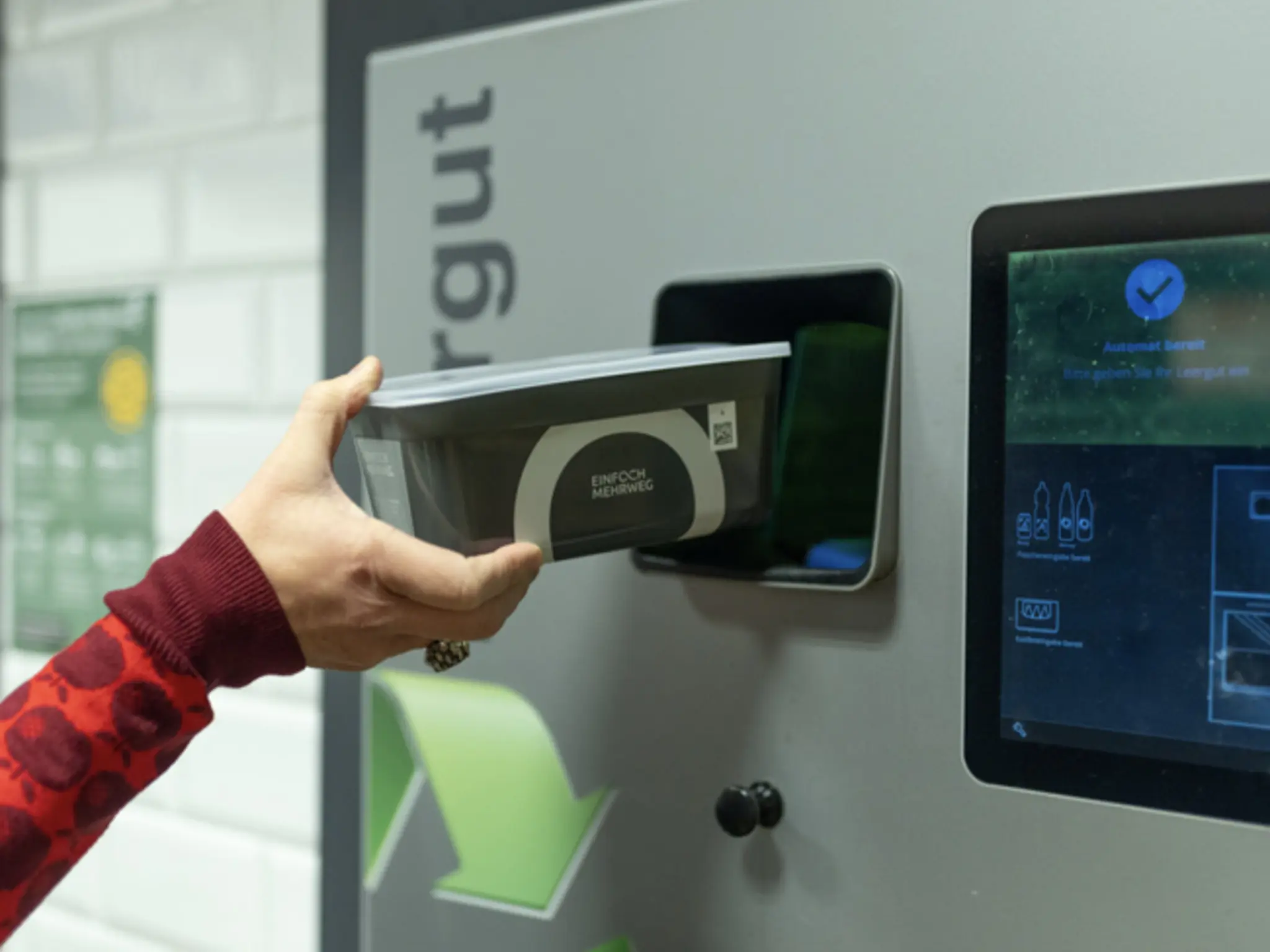 Hand gibt „Einfach Mehrweg“-Schale in einen Pfandautomaten