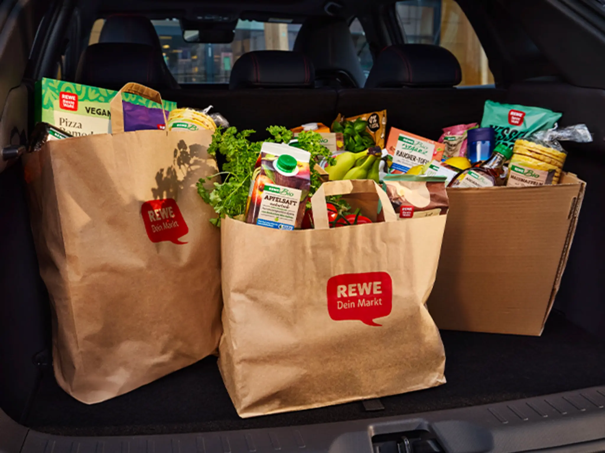Mehrere REWE Papier-Tragetaschen im Kofferraum eines Autos.