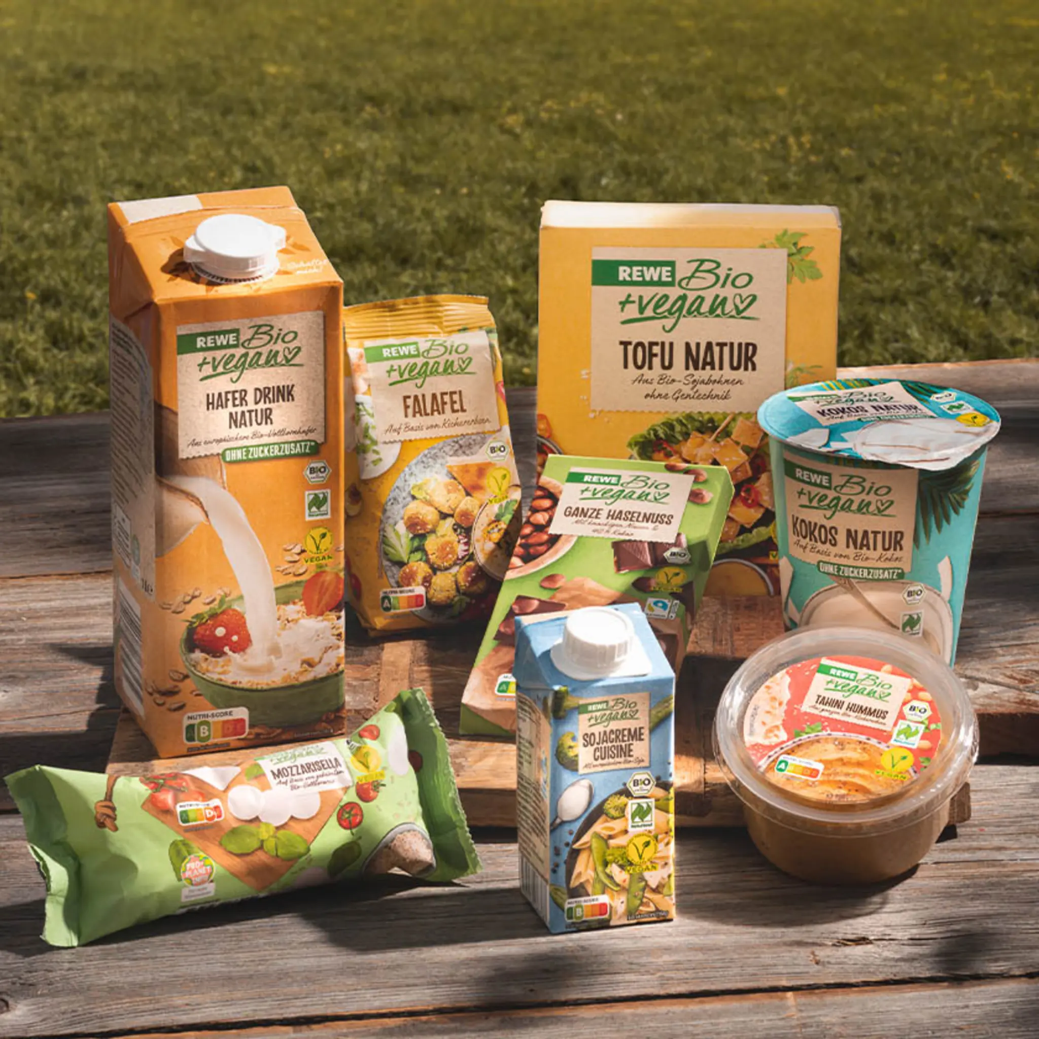Eine Auswahl unterschiedlicher REWE Bio + vegan Produkte steht auf einem Tisch: von pflanzlichem Mozzarella, über Tofu bis zum Soja-Drink.