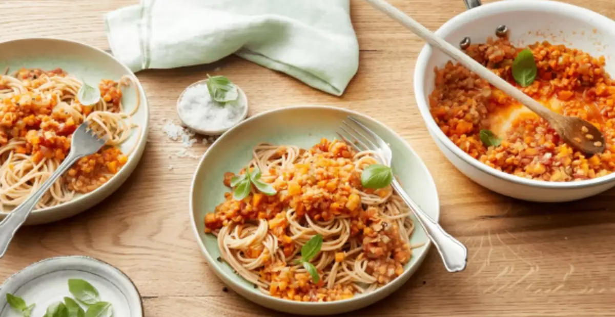Zwei Teller mit Spaghetti und Linsenbolognese, eine Pfanne mit Linsenbolognese, zwei kleine Teller mit Salz und frischem Basilikum. In der Mitte liegt eine Packung REWE Bio Vollkorn Spaghetti. 