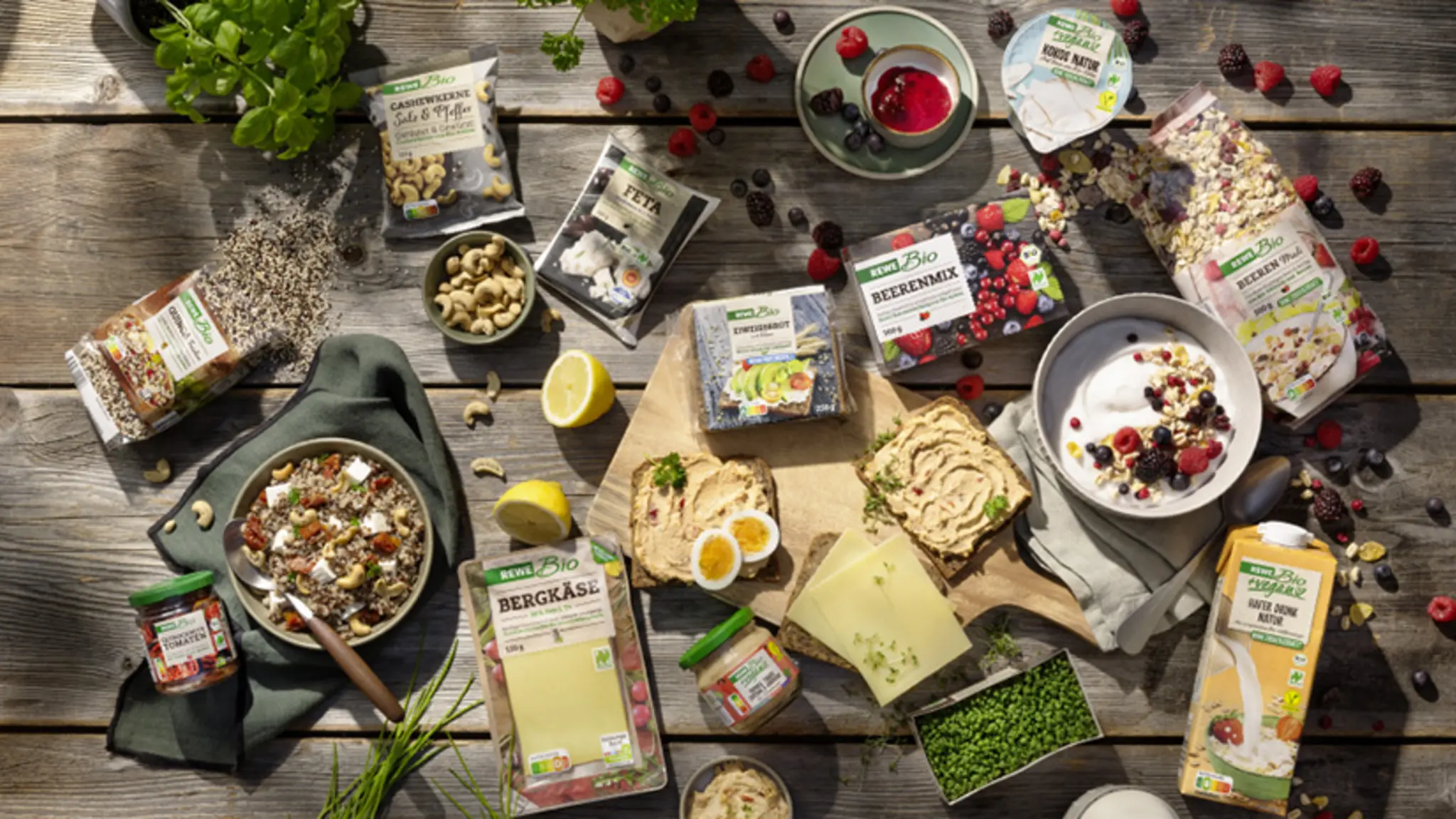Ein gedeckter Frühstückstisch. Zwischen Müslischalen und Schneidbrettern mit Brot liegen verschiedene REWE Bio Produkte. 