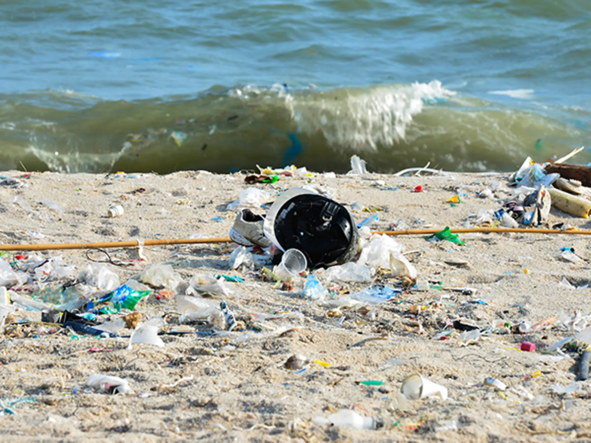 Eine Welle spült Plastikmüll an einen von Plastikabfällen übersäten Strand