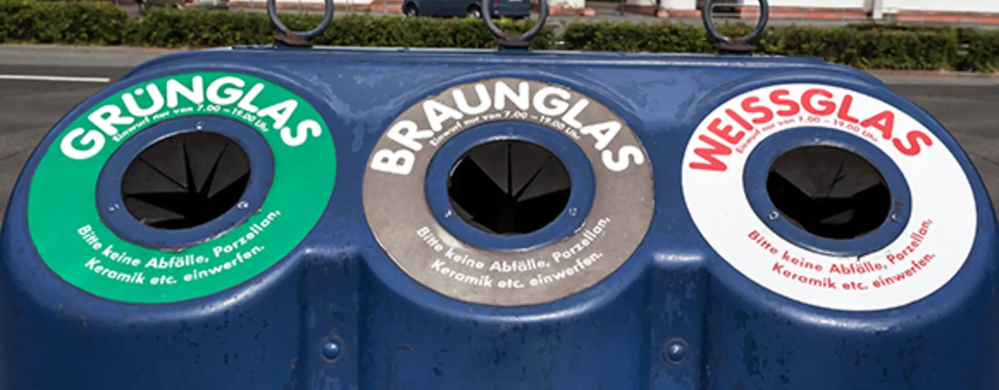 Ein blauer Altglascontainer am Straßenrand mit je einer Öffnung für Grünglas, Braunglas und Weißglas 