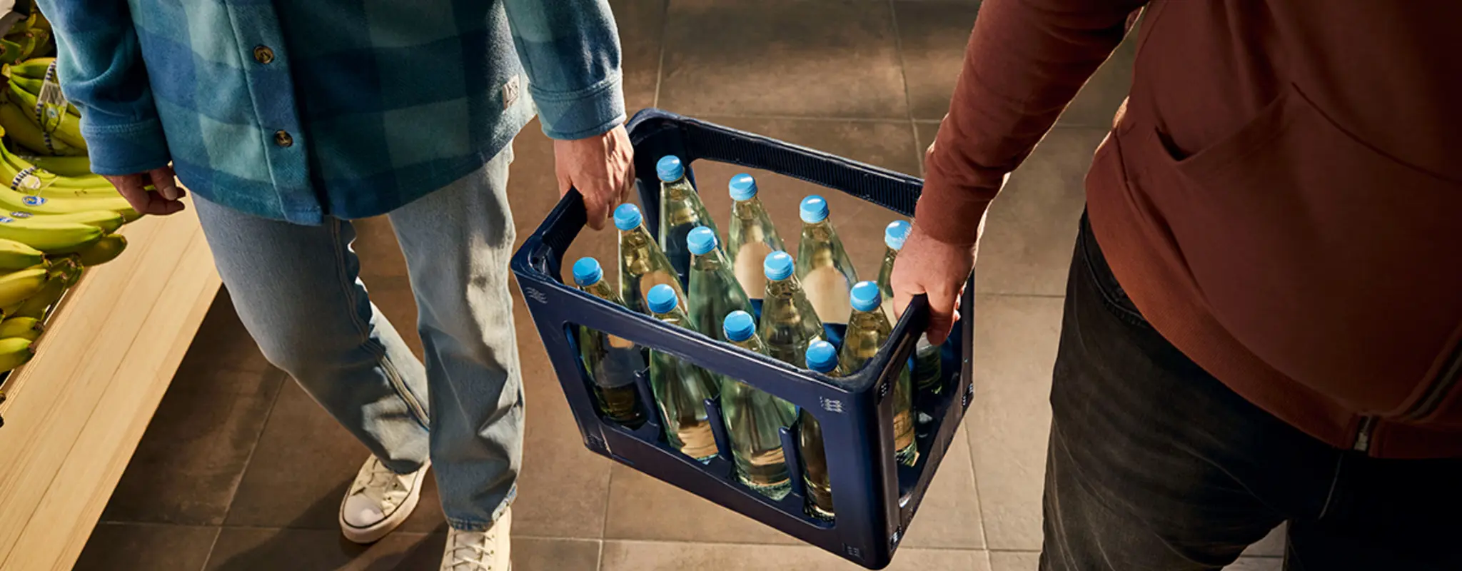 Zwei Männer tragen eine Wasserkiste mit Glasflaschen 