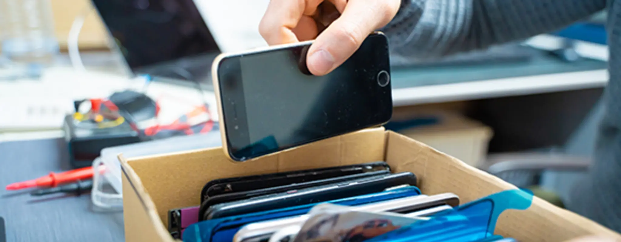 Eine Person legt ihr Smartphone in einen Karton voller Handys
