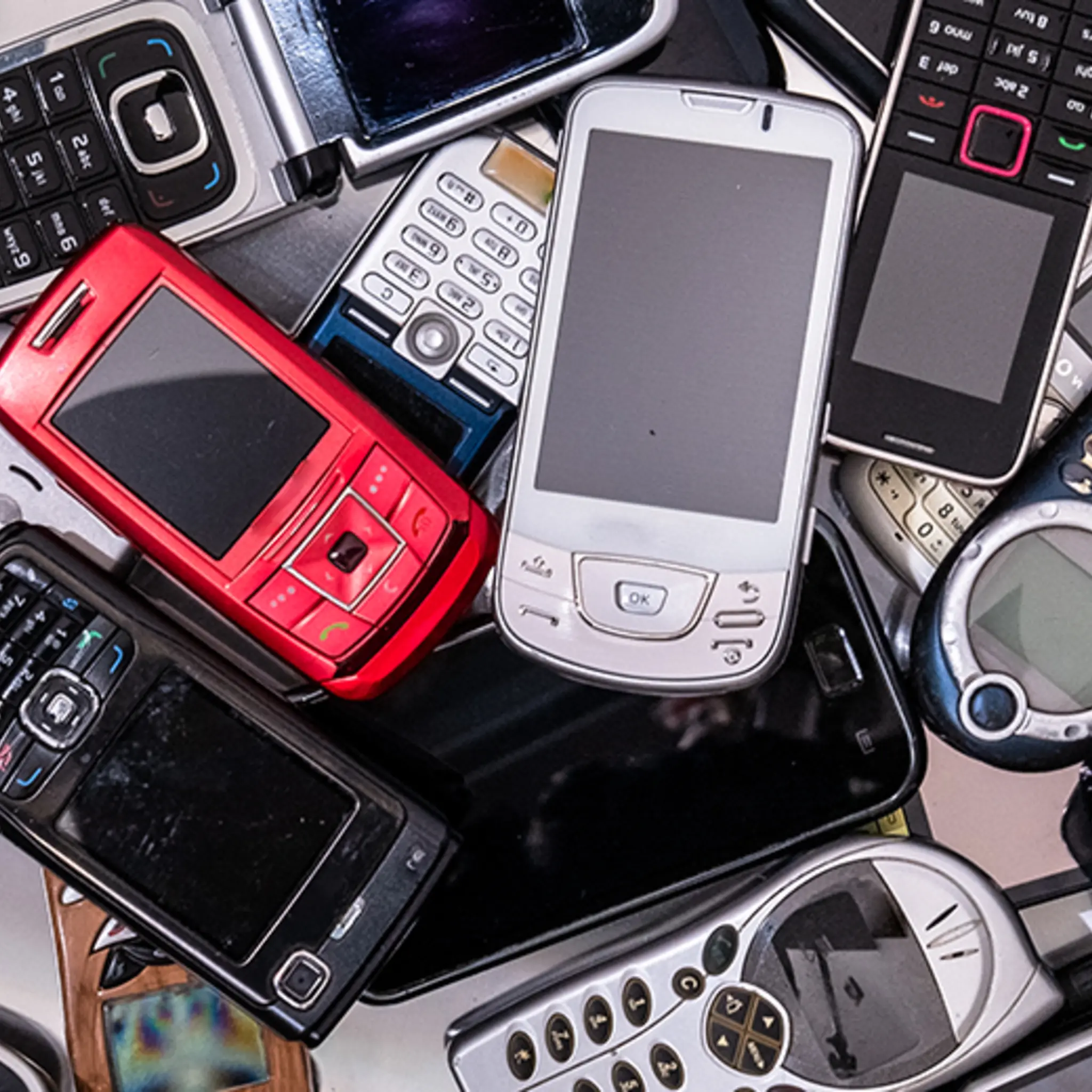Zwei Hände halten je ein Handy oder dessen Bestandteile vor eine grüne Recyclingtonne