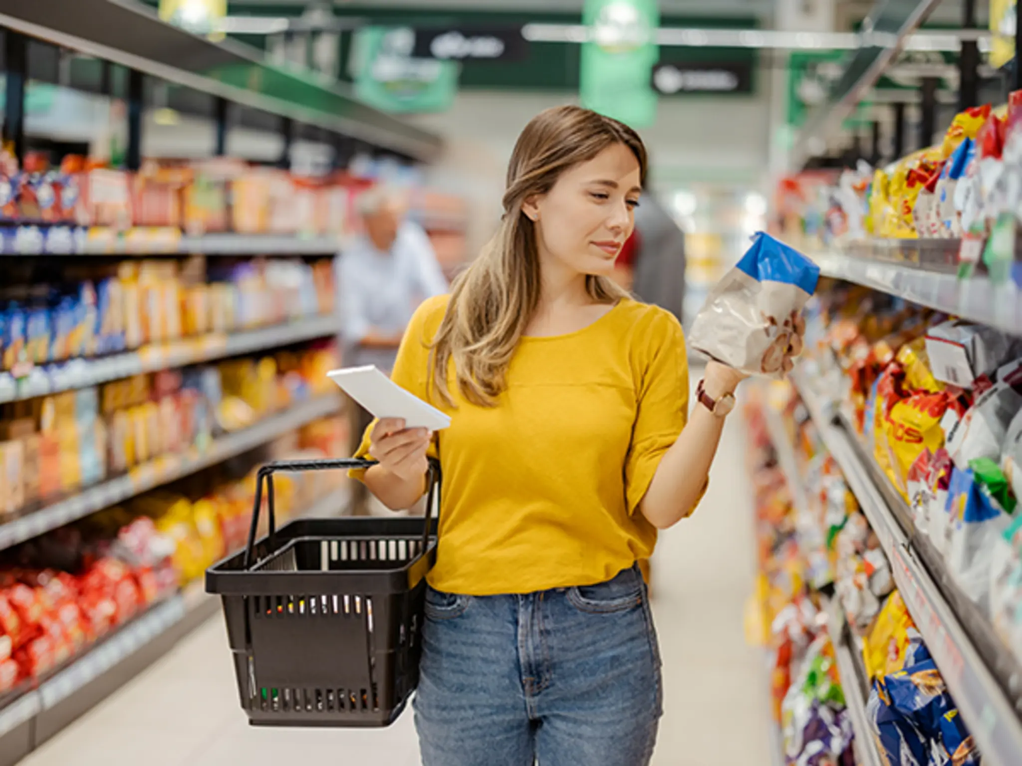 Eine lächelnde Frau im Jeanshemd legt in der REWE-Obstabteilung Äpfel in ein wiederverwendbares Obstnetz. 