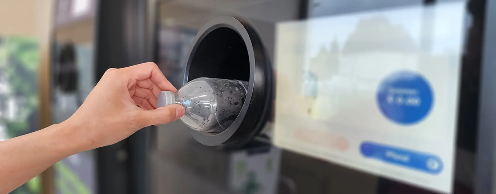 Eine Hand legt eine Plastikflasche in einen Pfandautomaten