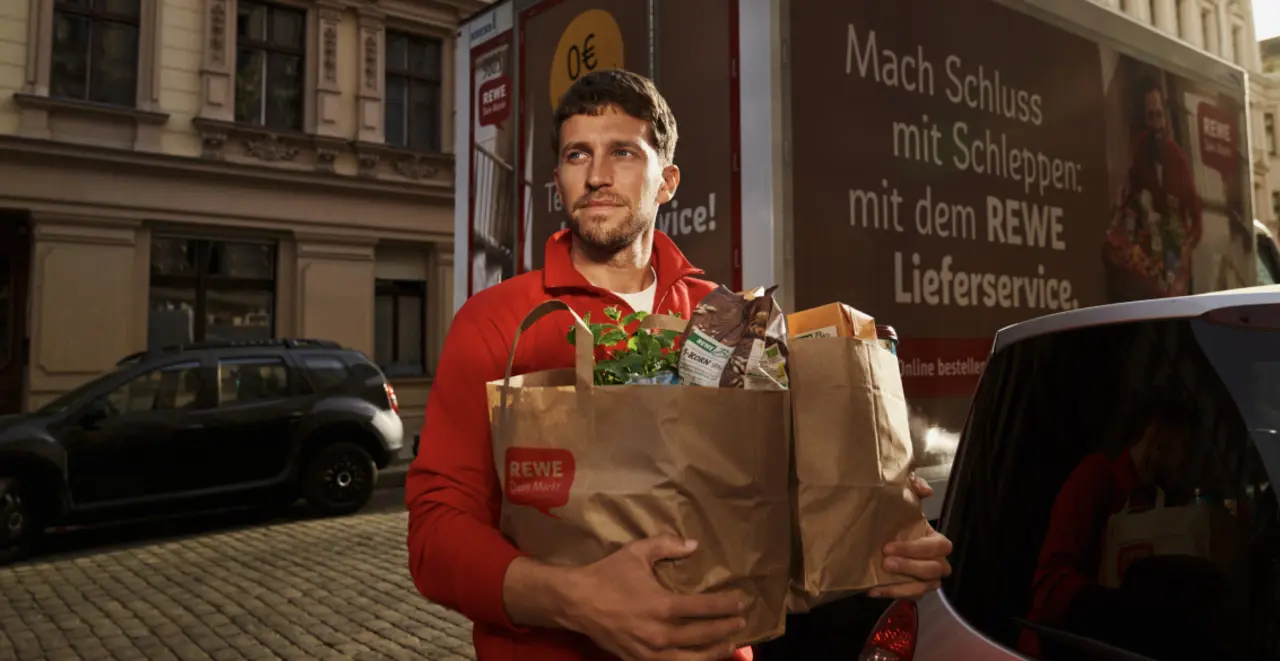 Ein REWE Lieferservice Mitarbeiter trägt Papiertüten mit einem Einkauf.