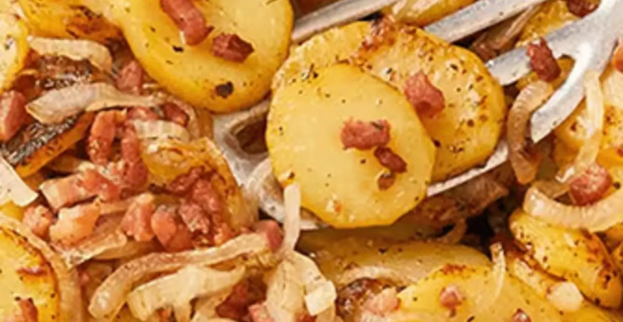 Eine Pfanne mit Bratkartoffeln steht auf einem Tisch. Ein Pfannenwender liegt in der Pfanne