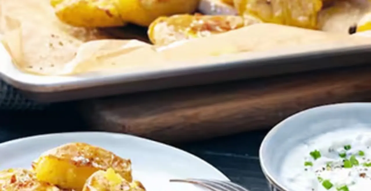 Auf einem gedeckten Tisch stehen zwei Teller mit Kartoffeln und Quark. Im Hintergrund steht ein Blech mit Kartoffeln.