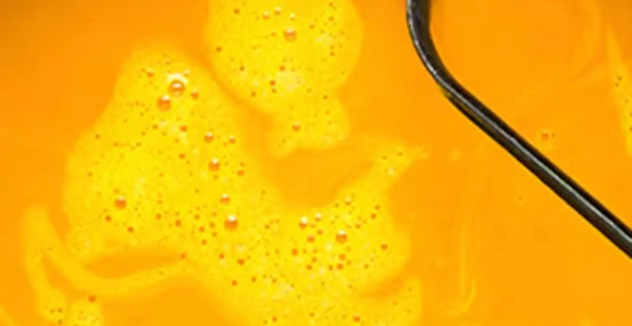 Eine großer Topf Kürbissuppe steht auf einem Tisch. Im Topf liegt eine Suppenkelle.