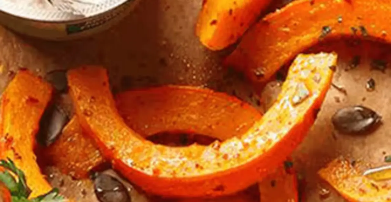 Auf einem Tisch steht ein Blech mit Kürbisspalten. Neben den Kürbisspalten steht eine Packung Körniger Frischkäse von REWE Bio.