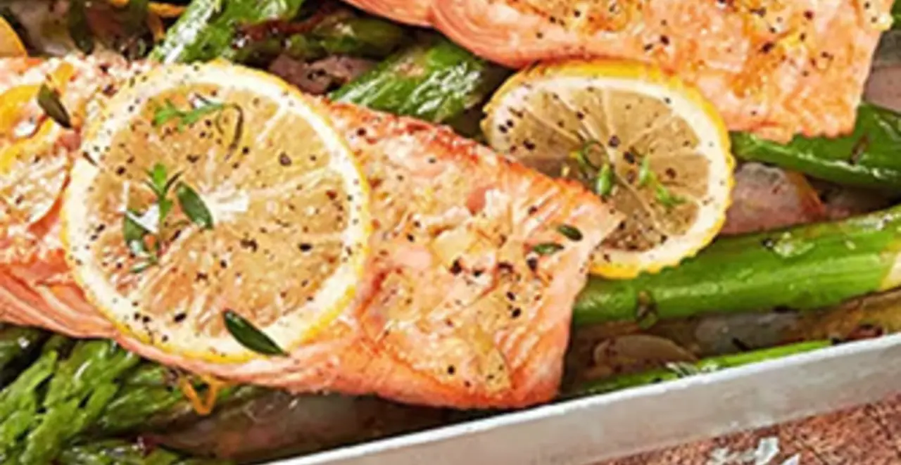 Ein Teller und eine Auflaufform mit Honig-Senf-Lachs und grünem Spargel steht auf einem Tisch. 