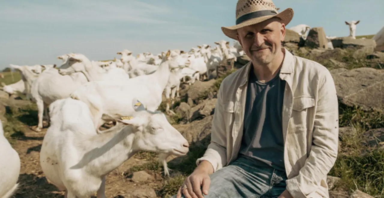 Franz Haslehner sitzt auf einem Felsen und beobachtet seine Ziegenherde. Die Tiere grasen auf einer Bergwiese. 