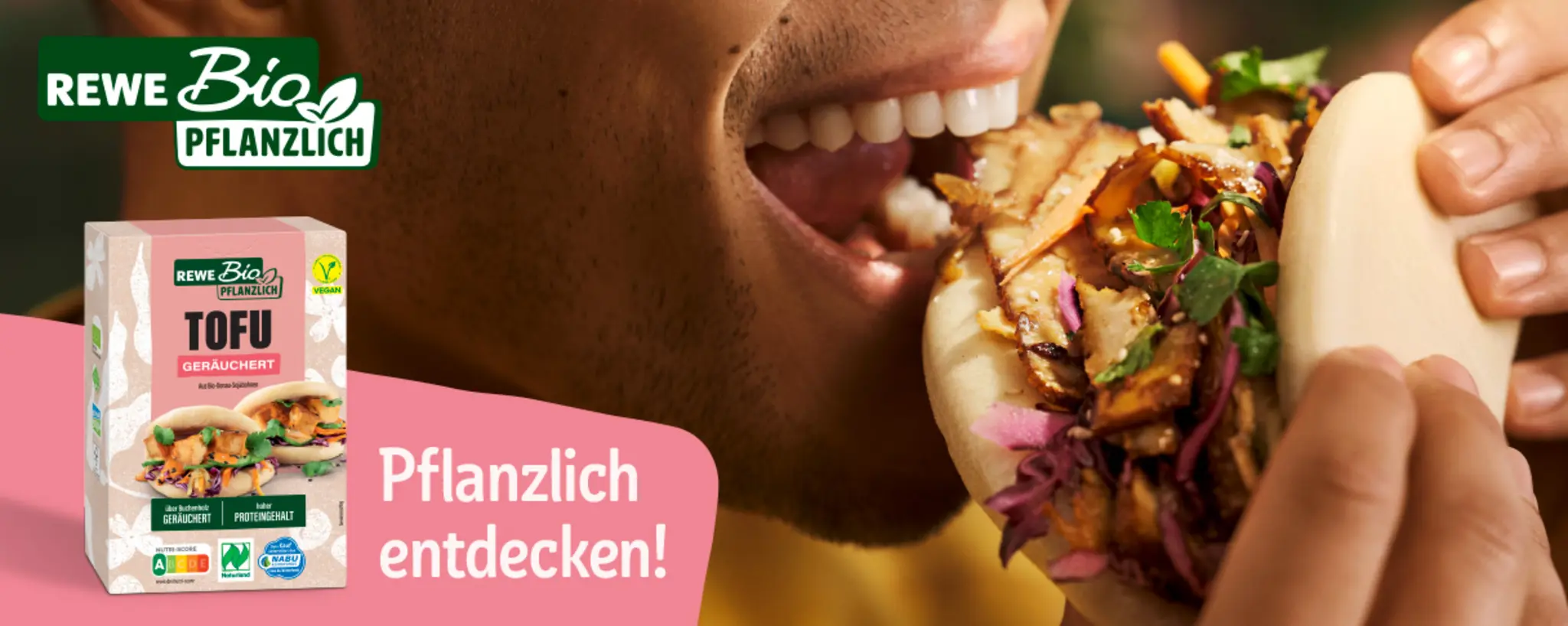Nahaufnahme einer Person, die in einen pflanzlichen Bao Bun beißt. Auf dem Bild steht das Logo „REWE Bio Pflanzlich“.