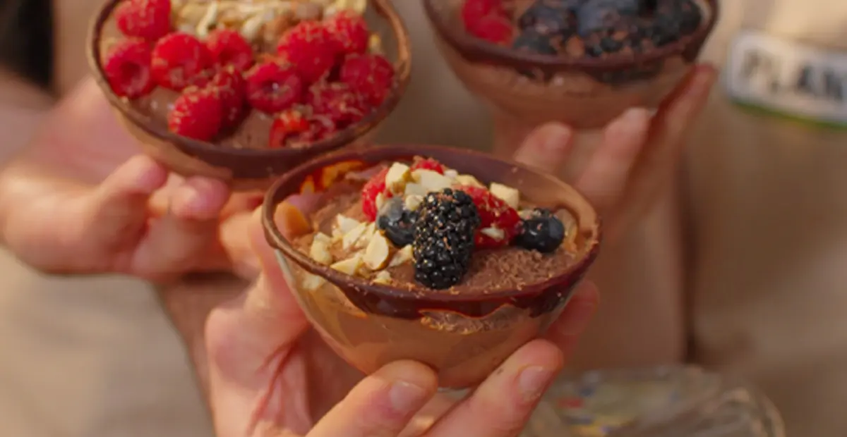 3 Schälchen veganes Schokoladen-Mousse – mit gemischten Beeren und gehackten Nüssen garniert. 