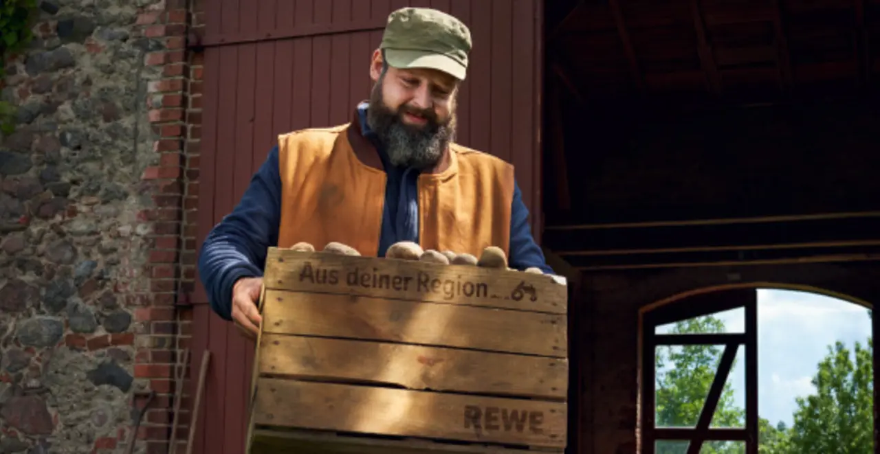 Ein Landwirt trägt eine große Kiste mit Kartoffeln.