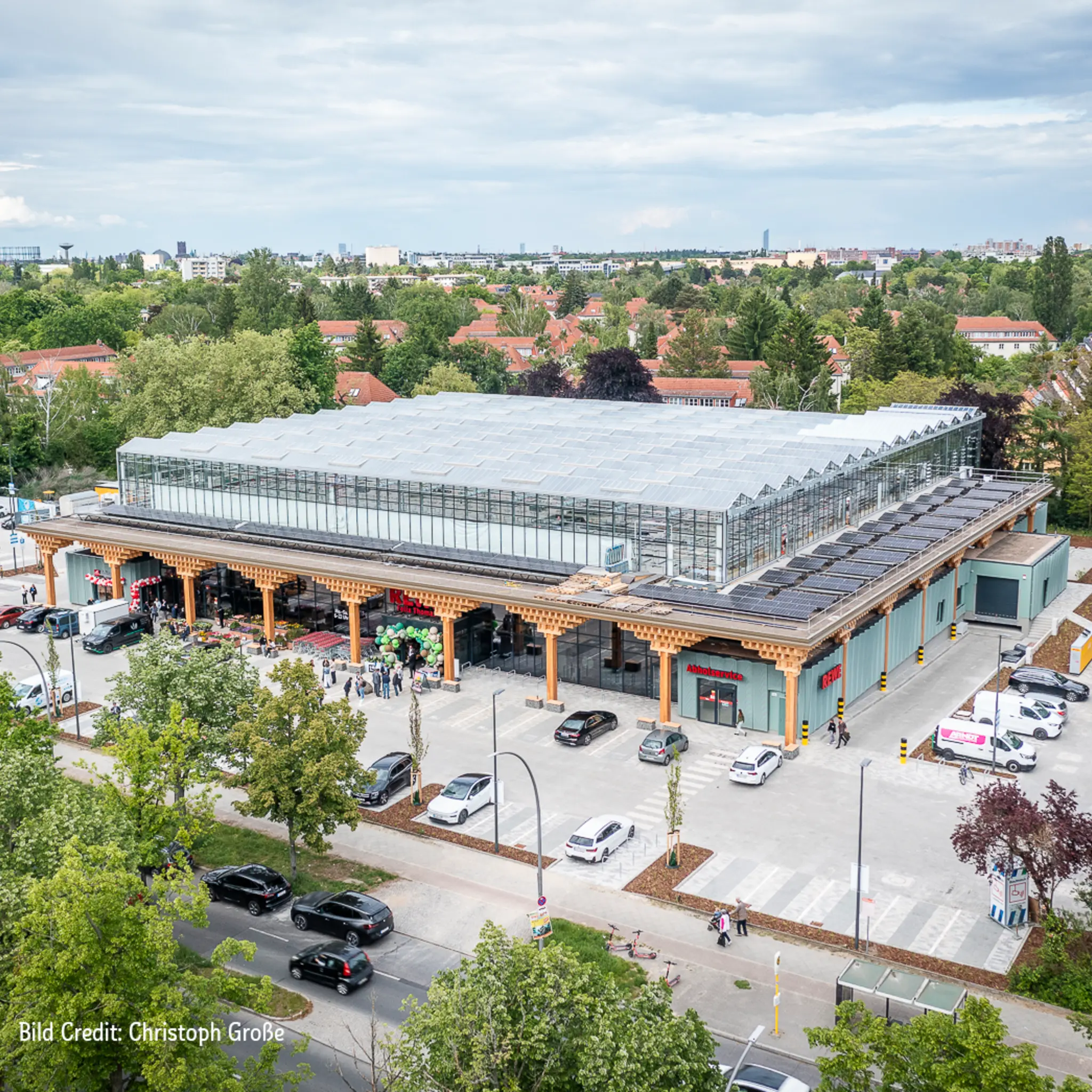 Der Eingang des Green Farming Marktes. Als Baumaterial wurde viel Holz eingesetzt. Vor dem Markt stehen Stände mit Blumen und Pflanzen.