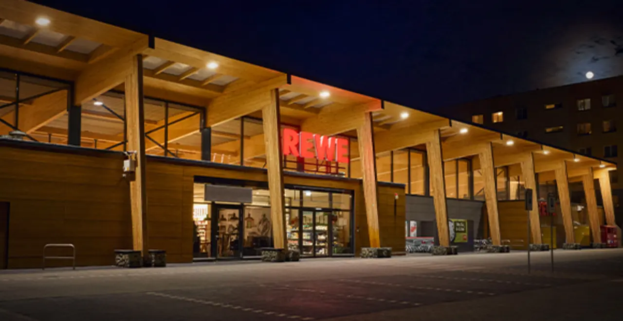 Ein hell erleuchtetes REWE Green Building bei Dunkelheit. 