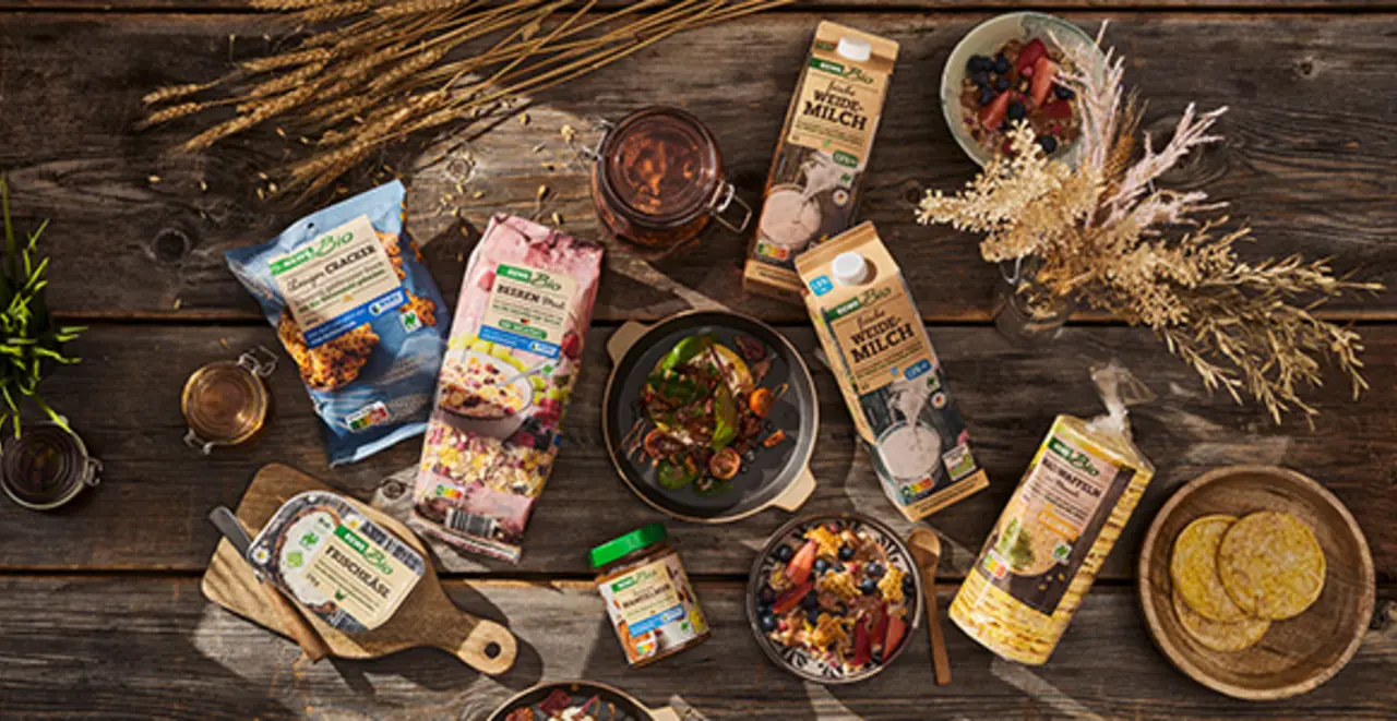 Verschiedene REWE Bio und REWE Bio + vegan Produkte liegen draußen auf einem Holztisch.