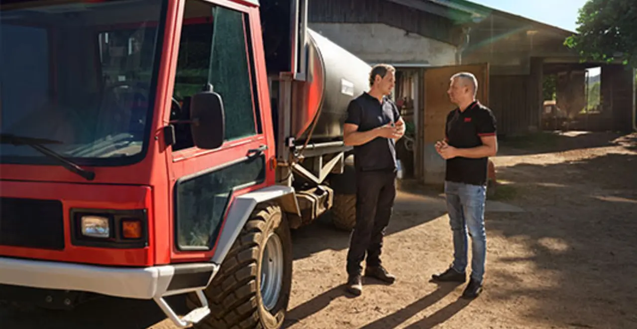 Landwirt David Engel und REWE Kaufmann Wladimir Pojanow vor einem Molkereiwagen auf Engels Betrieb. 